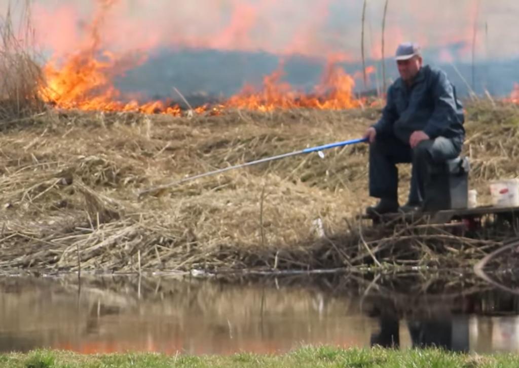 Hombre continúa pescando pese al incendio detrás de él