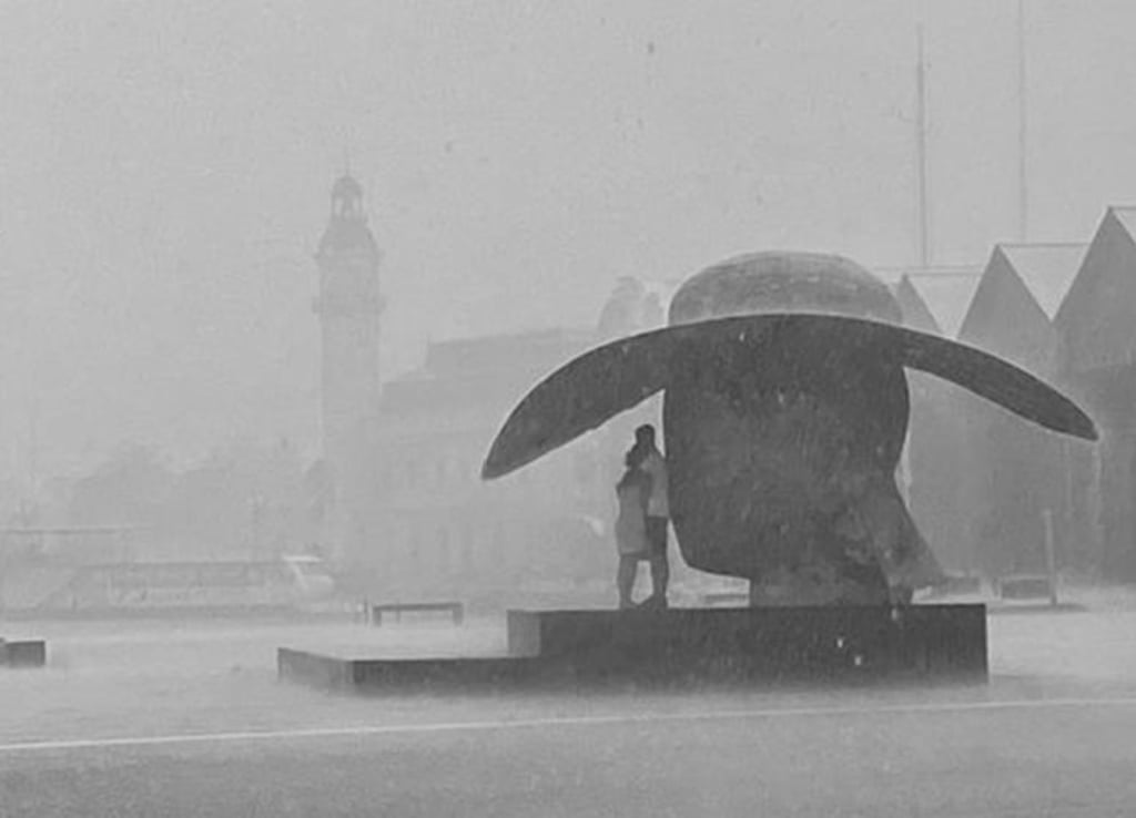 Fotografían a pareja de Valencia resguardándose de la lluvia bajo una escultura