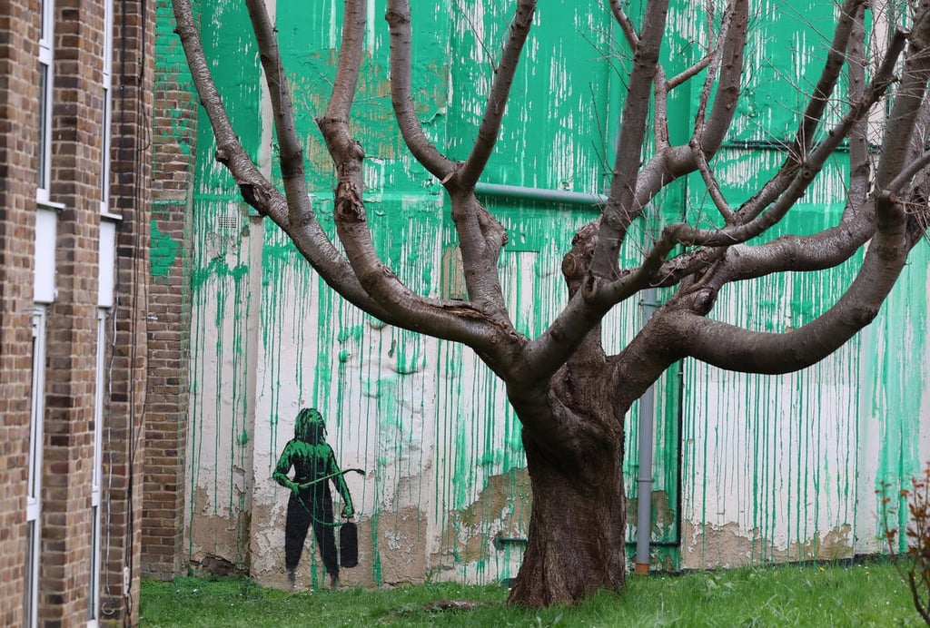Mural. La obra está hecha detrás de un gran árbol, para dar la apariencia de hojas de color verde, y junto a él se ve el dibujo de una persona que sostiene una manguera a presión.