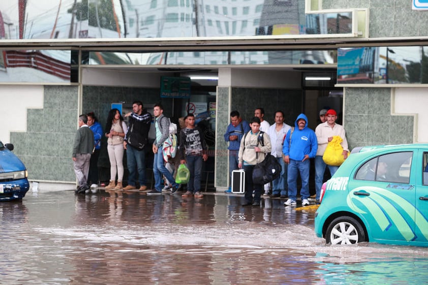 Usuarios de la central camionera aguardan ante las inundaciones a las afueras de la la estación.