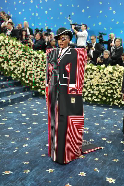 Janelle Monáe con un traje con capa larga y parches rojos.