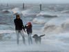 Un padre, su hija y su caminar perro en una playa durante los fuertes vientos y las olas de trituración en el puerto de ferry de Neuharlingersiel, Alemania.